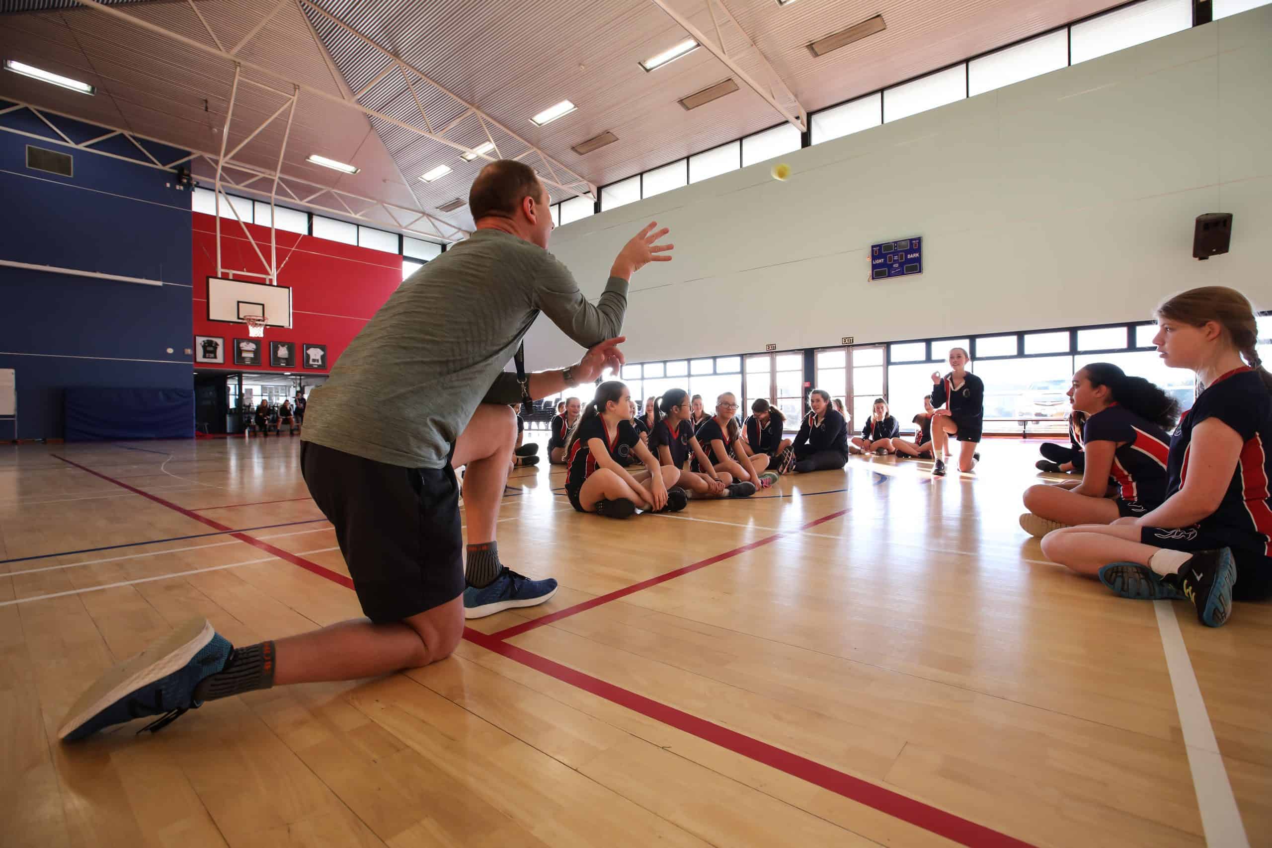 Teacher demonstrating a ball throwing technique to female students in a school gymnasium